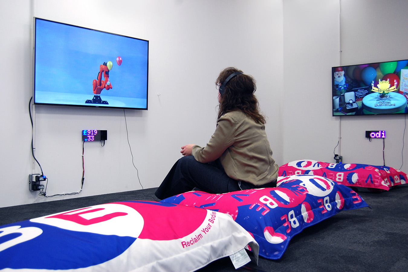 alt: Woman sat on a BEV cushion watching the videos created by the artists, the longer she sits the more the price of the artwork decreases