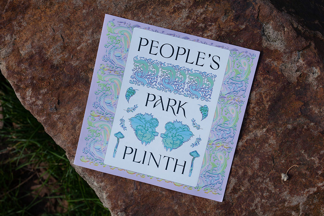 alt: The People's Park Plinth booklet is shown laying on a rock inside Finsbury Park