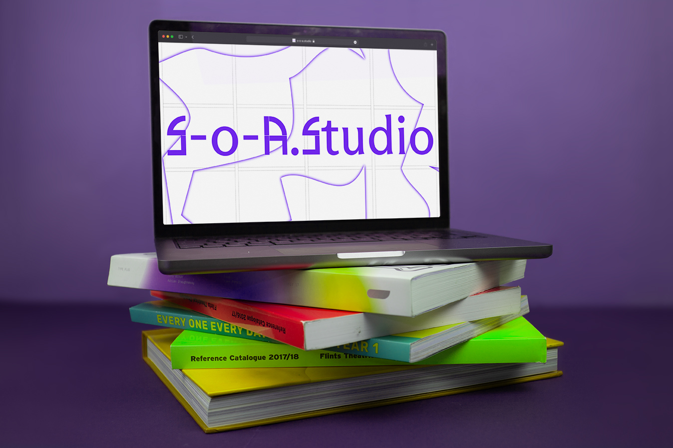An image of a laptop sitting ontop of some art books, the laptop has the S-O-A studio website on its display