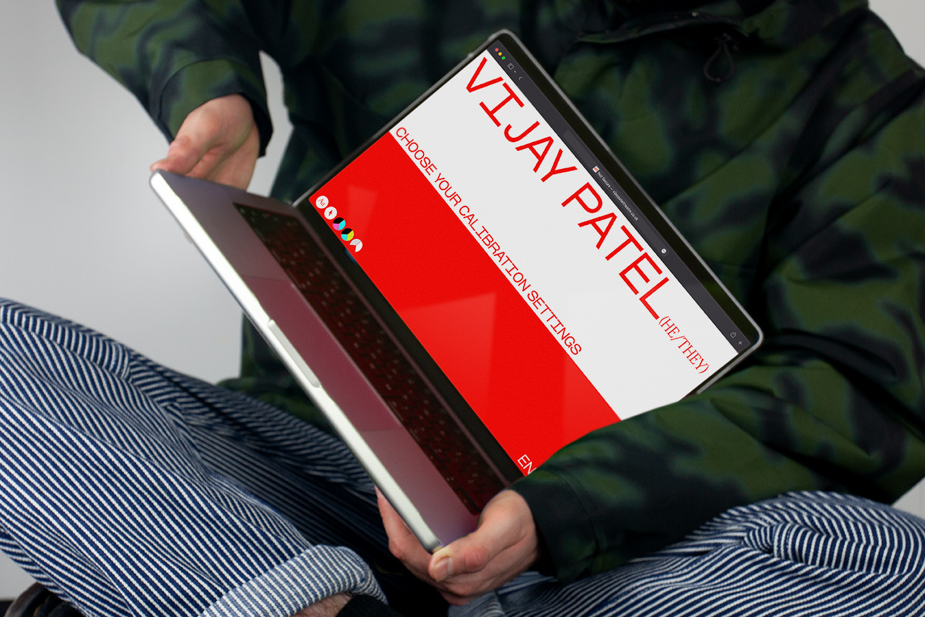 A person sitting holding a laptop on their lap, the laptop screen shows Vijay Patels website homepage